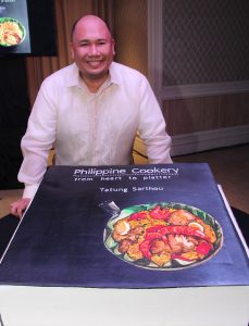 Chef Myke 'Tatung' Sarthou standing before the cake version of his book's cover